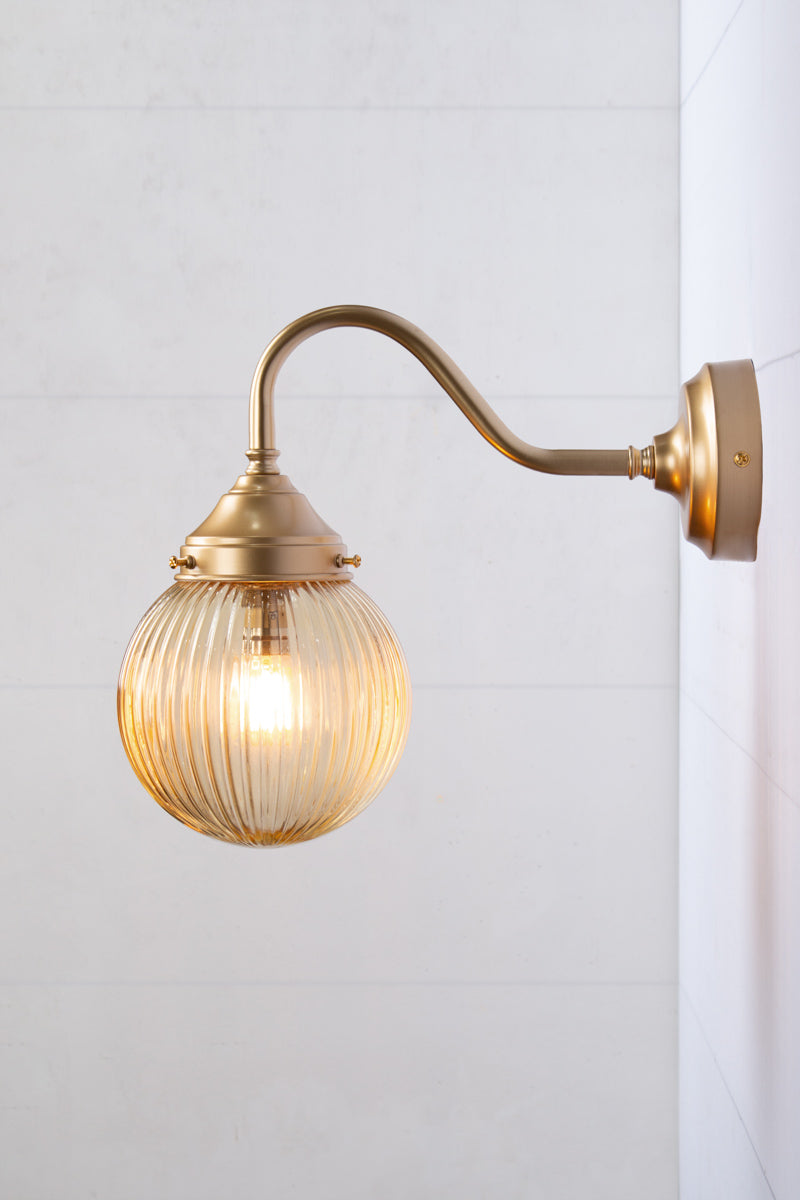 Exterior wall light with a gold/brass gooseneck arm and amber reeded shade, side view.