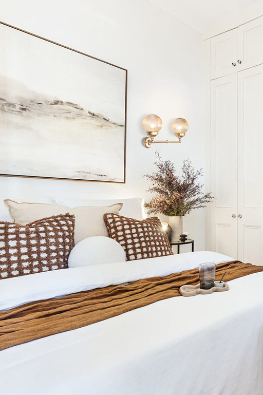 Two amber reeded glass ball shades on a double gold/brass straight arm sconce in a bedroom. 