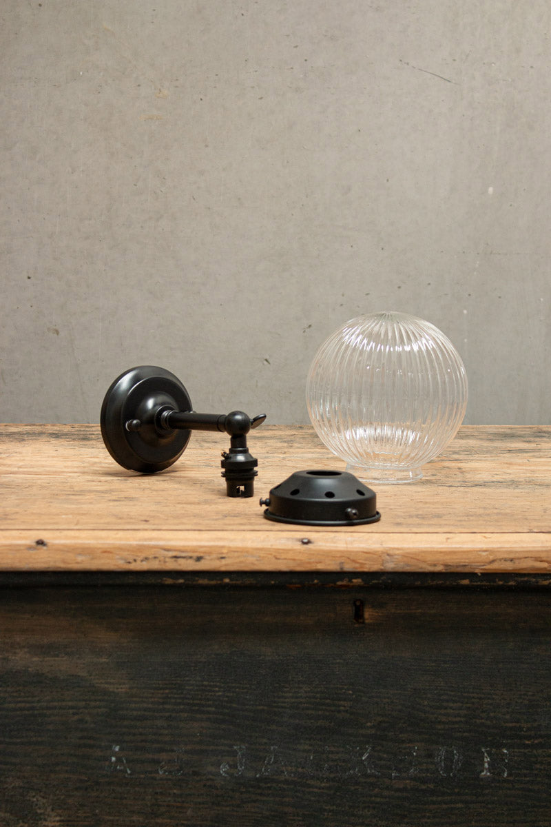 Disassembled clear reeded glass ball light with black gallery and short straight arm. 