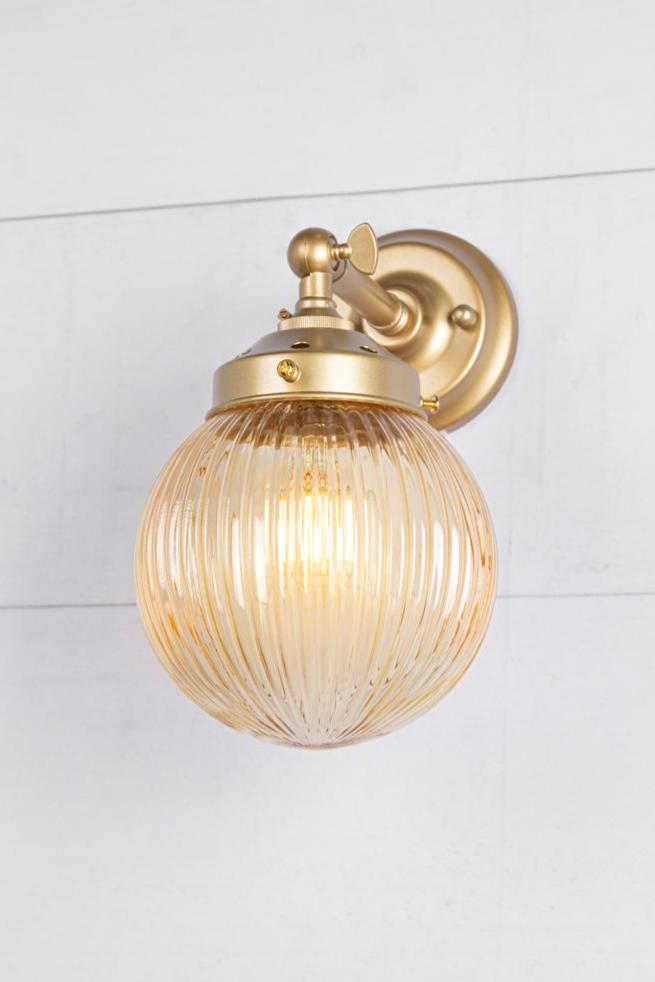 Front view of a Amber glass reeded ball shade on a short gold/brass swivel straight arm.