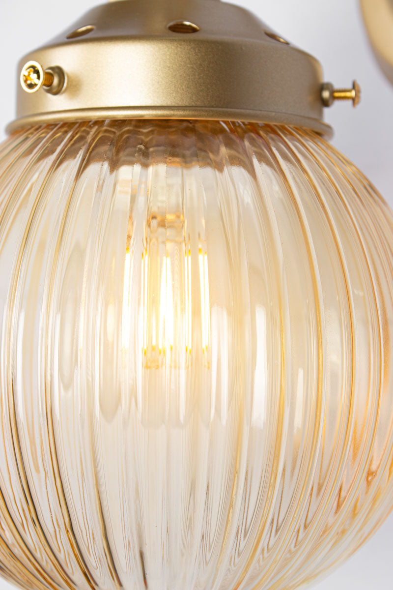 Close up of a Amber glass reeded ball shade on a short gold/brass swivel straight arm.