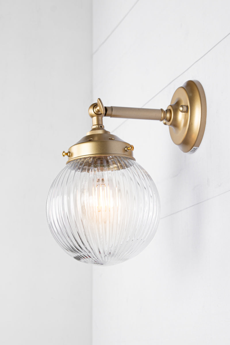 Side view of clear glass reeded ball shade on a short gold/brass swivel straight arm.