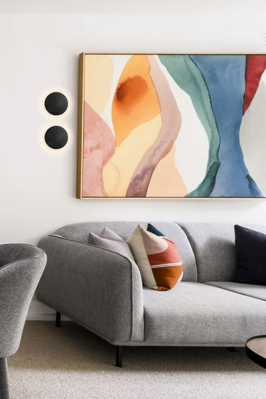 Two small black circular wall lights next to a colourful painting in aa lounge room.