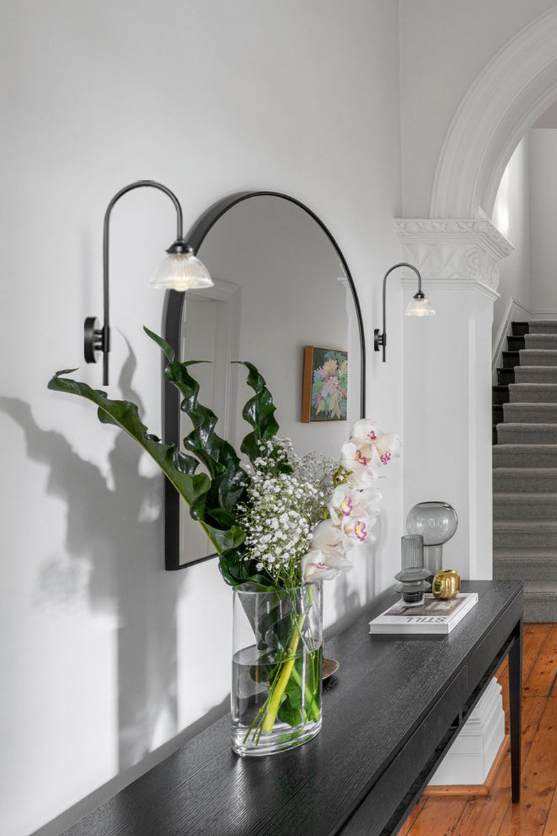 Two black shepherds hook wall sconces with glass shades in an entry way.