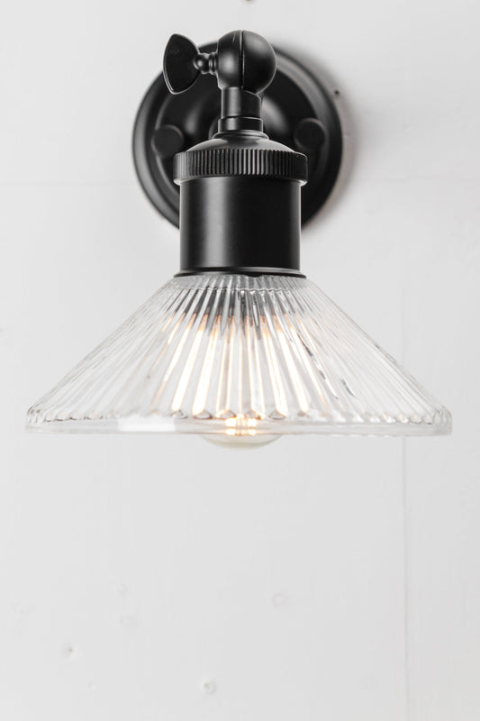 Glass shade with delicately pleated pattern on black wall sconce