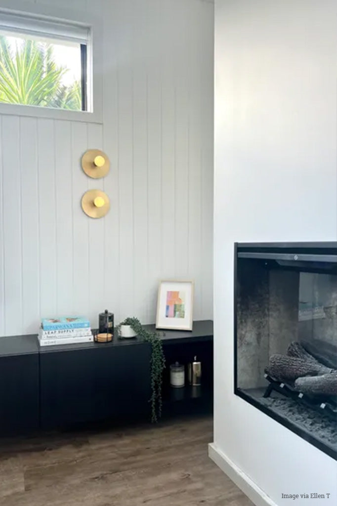 Two wall sconces with brass discs and opal bulbs installed in a white room with fireplace. 