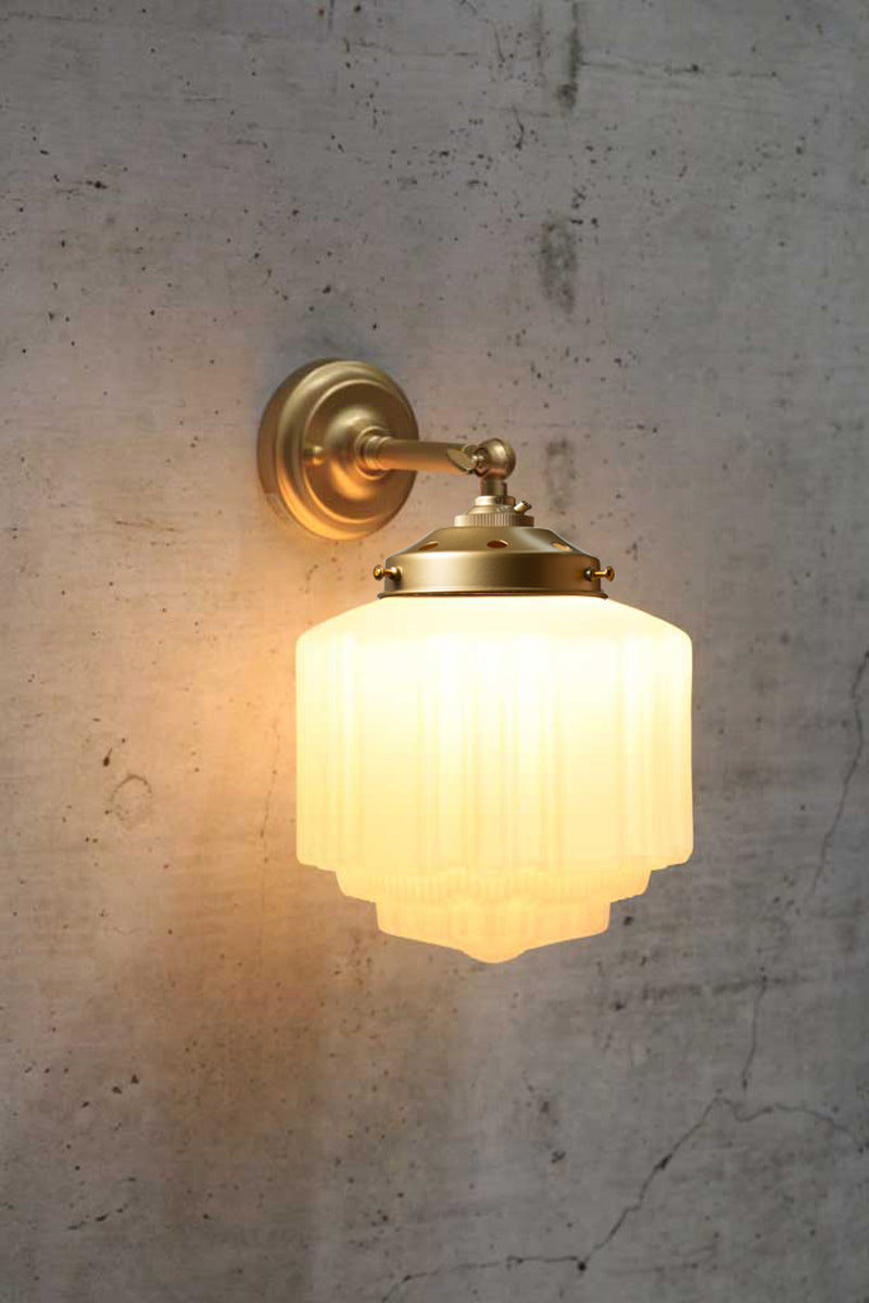 Short straight arm wall sconce in gold/brass with a Deco schoolhouse glass shade. 