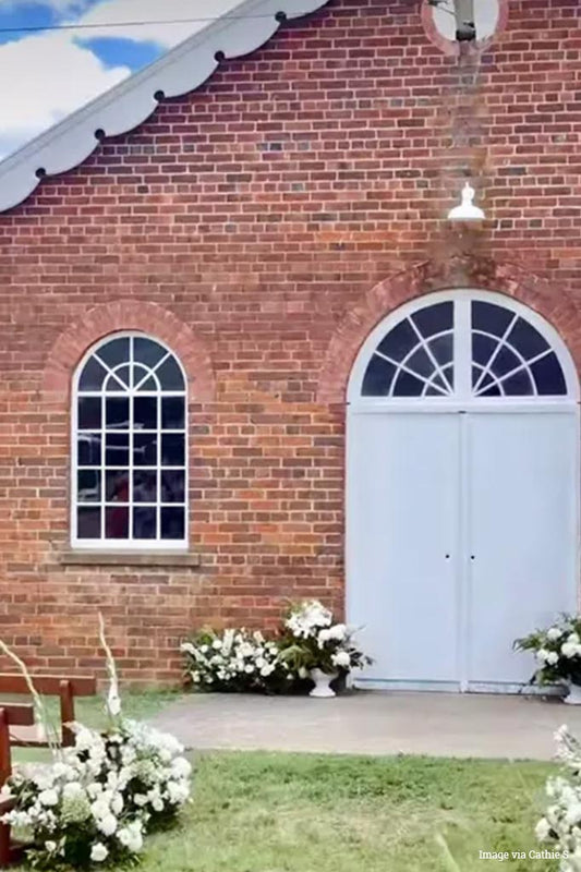 White warehouse shade on white gooseneck arm above an arched doorway on a red brick building. 