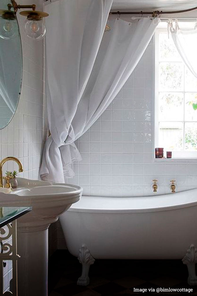 gold/brass disc wall light with clear ball shade next to a mirror inside of a bathroom