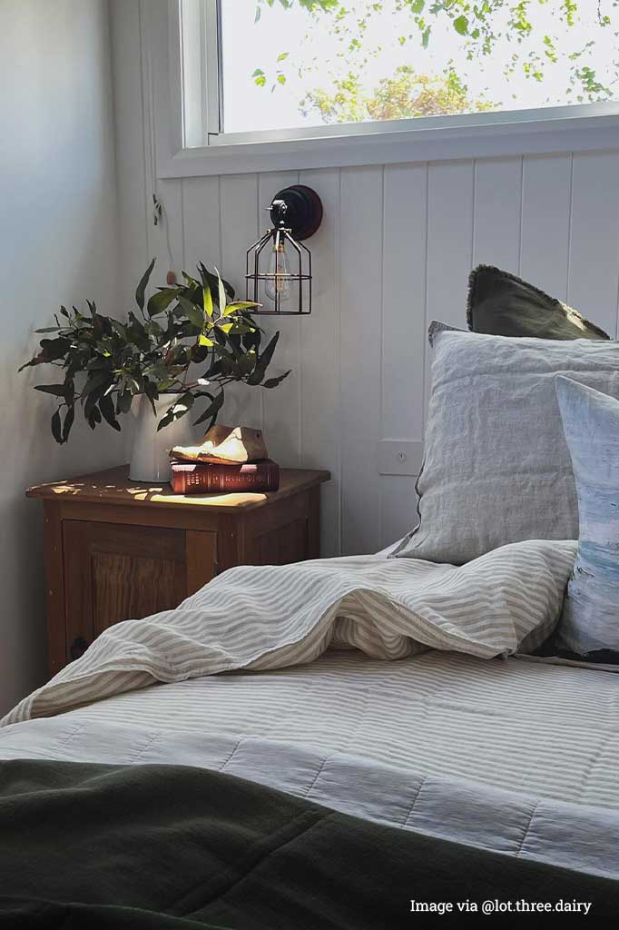 Black round cage wall light with small shade over bedside table.