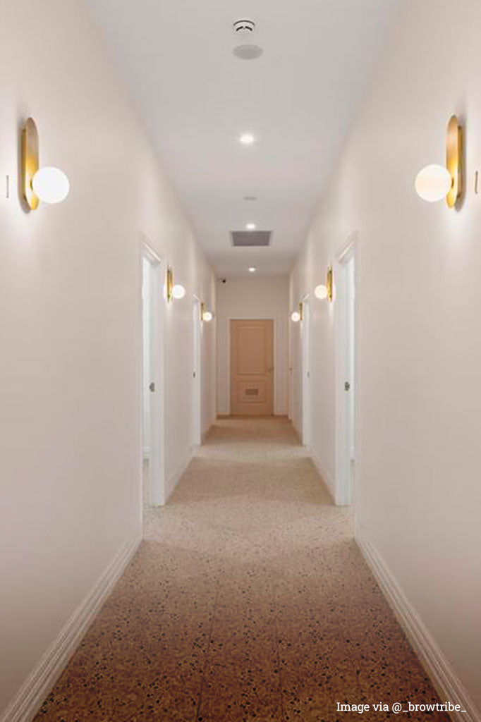 Opal wall light with gold wall plate in a hotel hallway.