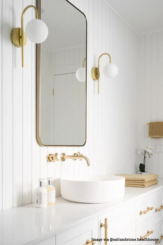 Two gold hook wall sconces with opal round shades hanging either side of a bathroom mirror.