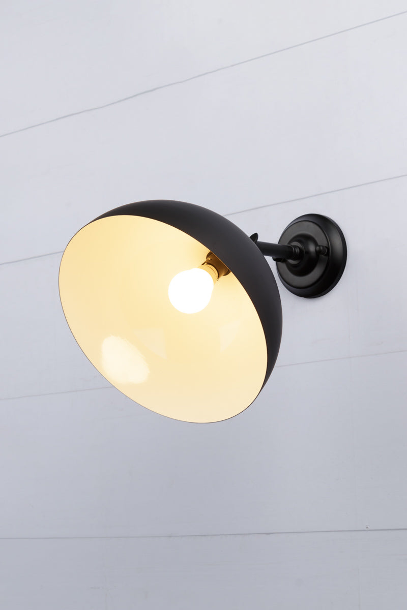 Small black dome shade tilted on a steel black straight arm wall sconce