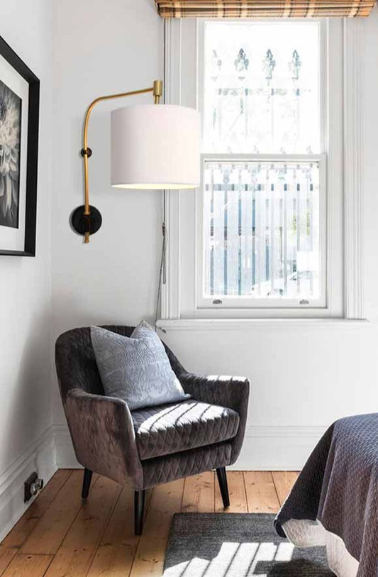 Wing arm wall light with white fabric shade in a bedroom.