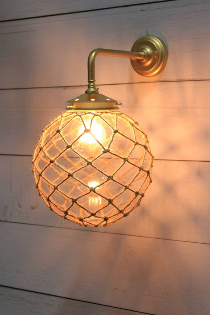 Medium, clear glass ball shade with rope detail on a 90 degree arm wall sconce in gold/brass. 