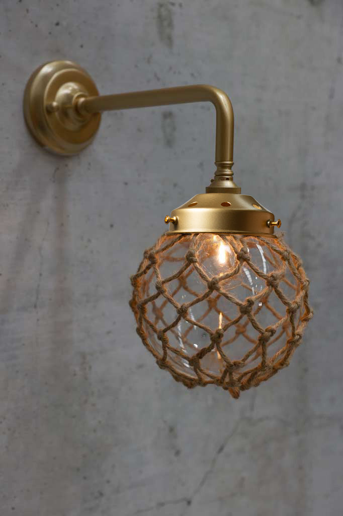 Small, clear glass ball shade with rope detail on a 90 degree arm wall sconce in gold/brass. 