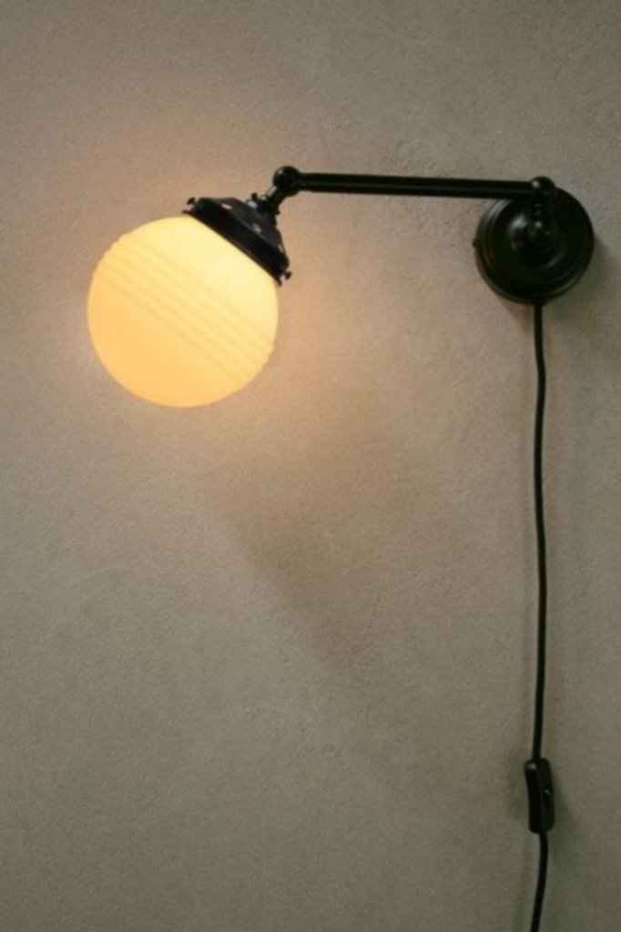 Opal ridged glass ball shade on black adjustable wall sconce with wall plug. 