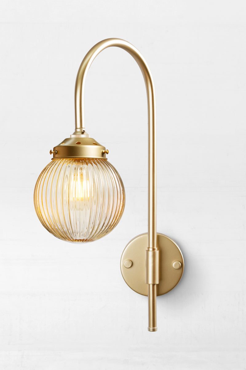 Shepard gooseneck wall light in gold/brass with an amber reeded glass ball shade. 