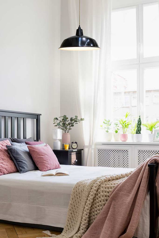 Black pendant light with jute cord suspended above a bed.