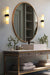 Two Cheswick vanity lights hanging next to a large circle mirror in a bathroom. 