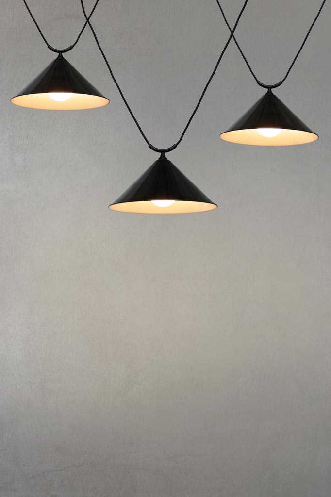 Three large black steel cone shades on trapeze pendant cords.