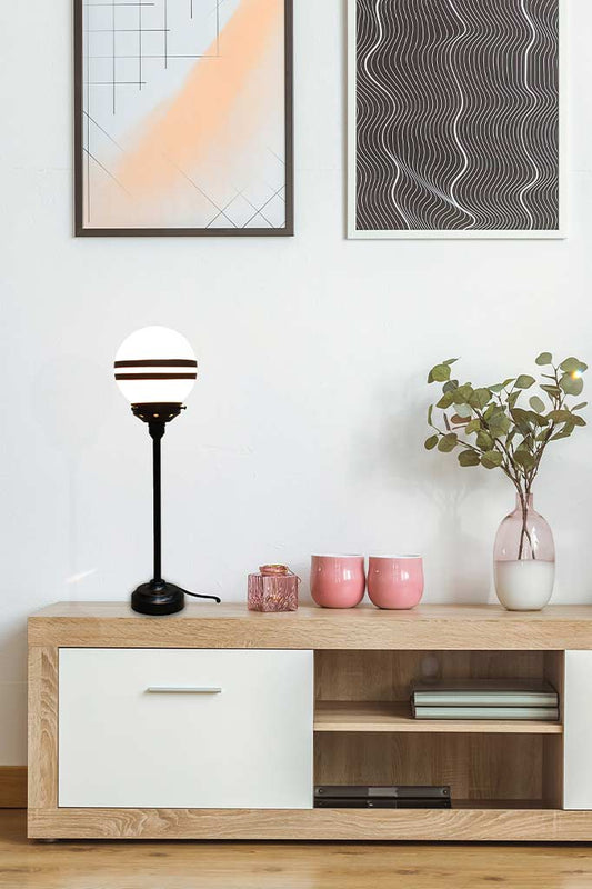 Matt black large candlestick table lamp with two stripe shade over a tv unit.