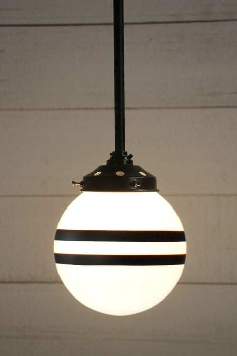 Hand painted opal glass ball pendant light with two stripes hung from black steel pole. 