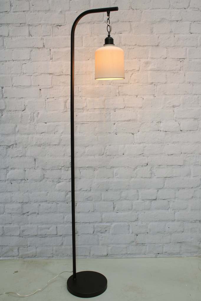 Floor lamp with black finish against brick wall. 