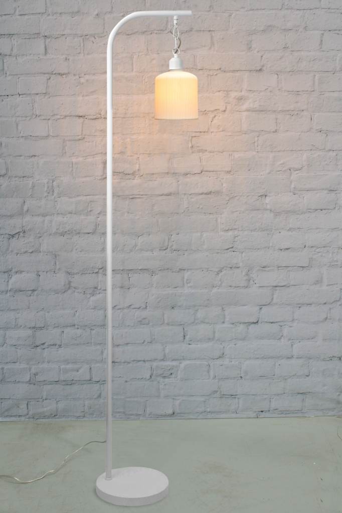 Floor lamp with white finish against brick wall. 