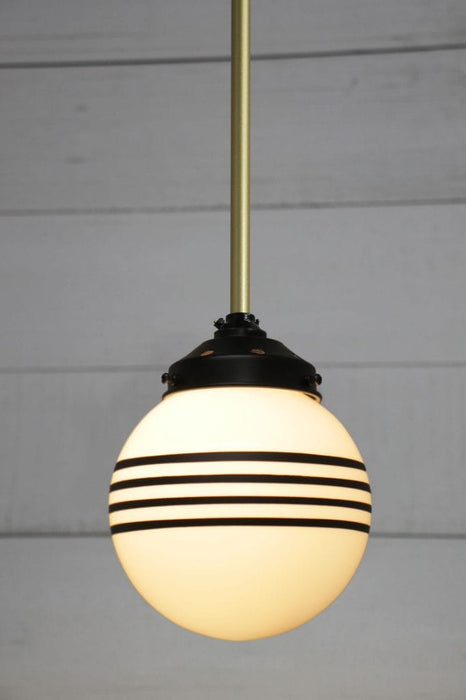 Hand painted opal glass ball pendant light with four stripes hung from gold steel pole. 