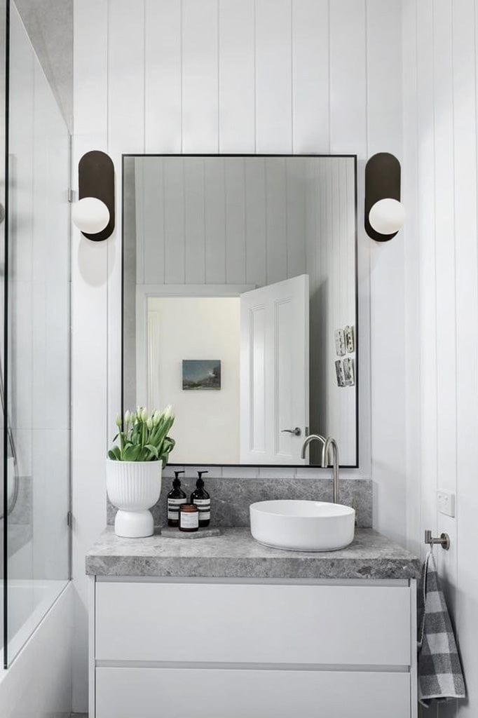 Two opal wall lights mounted on slim black metal plates hung on either sides of a bathroom mirror. 