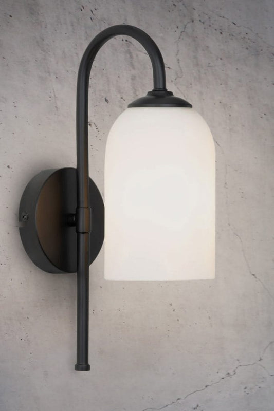 Wall light with cylindrical opal glass shade and black metalware build affixed on textured wall. 