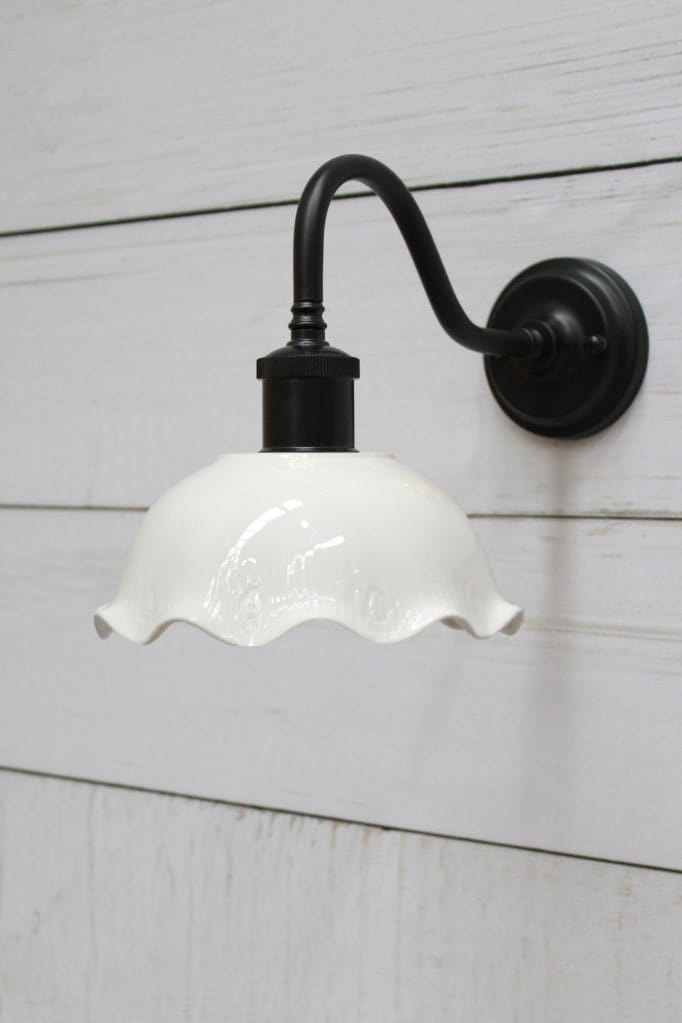 Ceramic gooseneck wall light with black arm affixed on wall. 