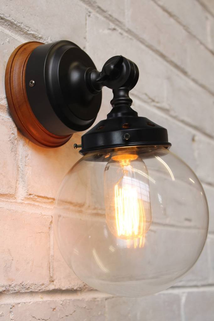 Black metal wall light with clear shade and natural wood mounting block on white brick background