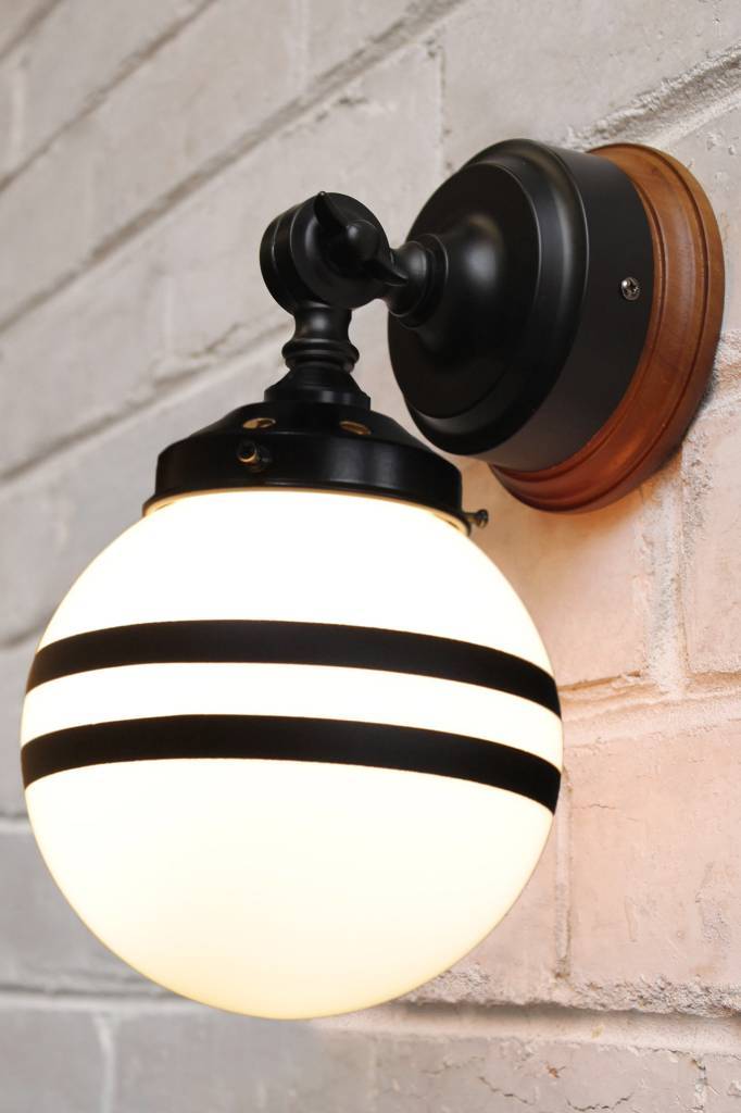 Black wall light with natural wood mounting block and opal shade with two stripes against a concrete background