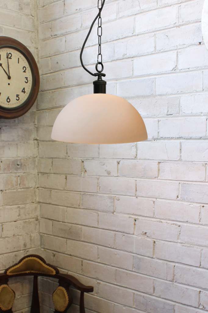 Small opal glass pendant with a black pendant chain against a white brick wall