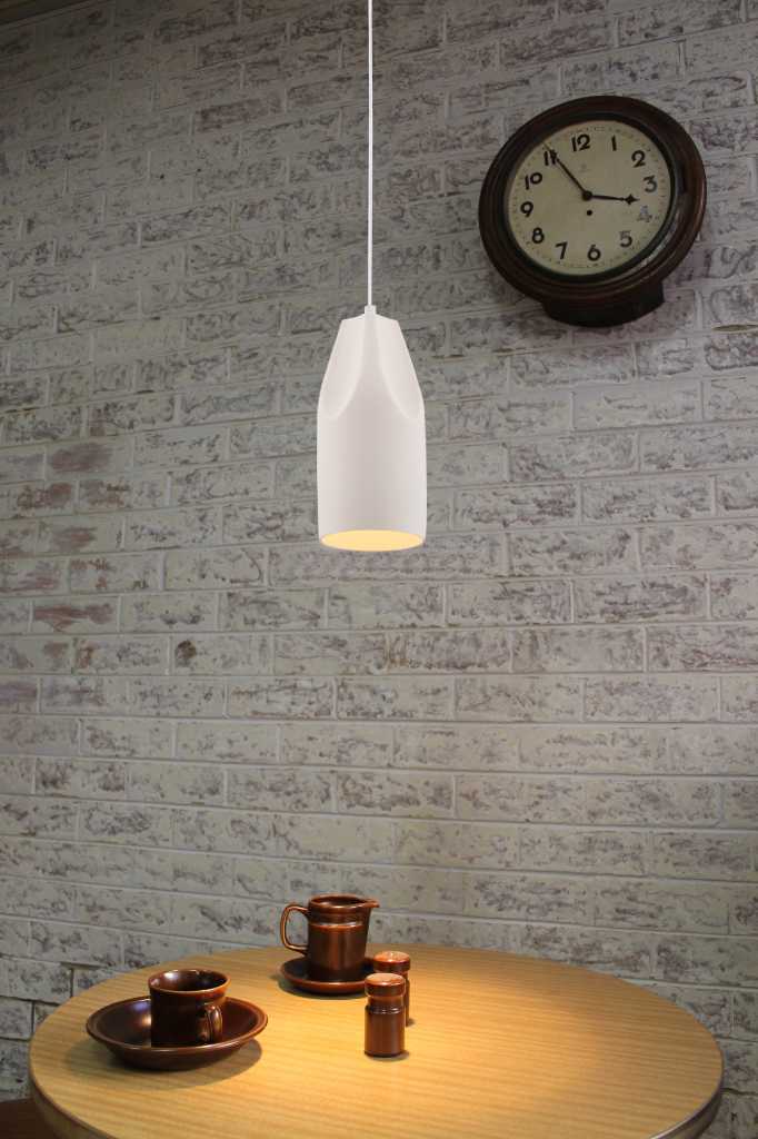 White metal pendant above a timber laminate table with a white brick background